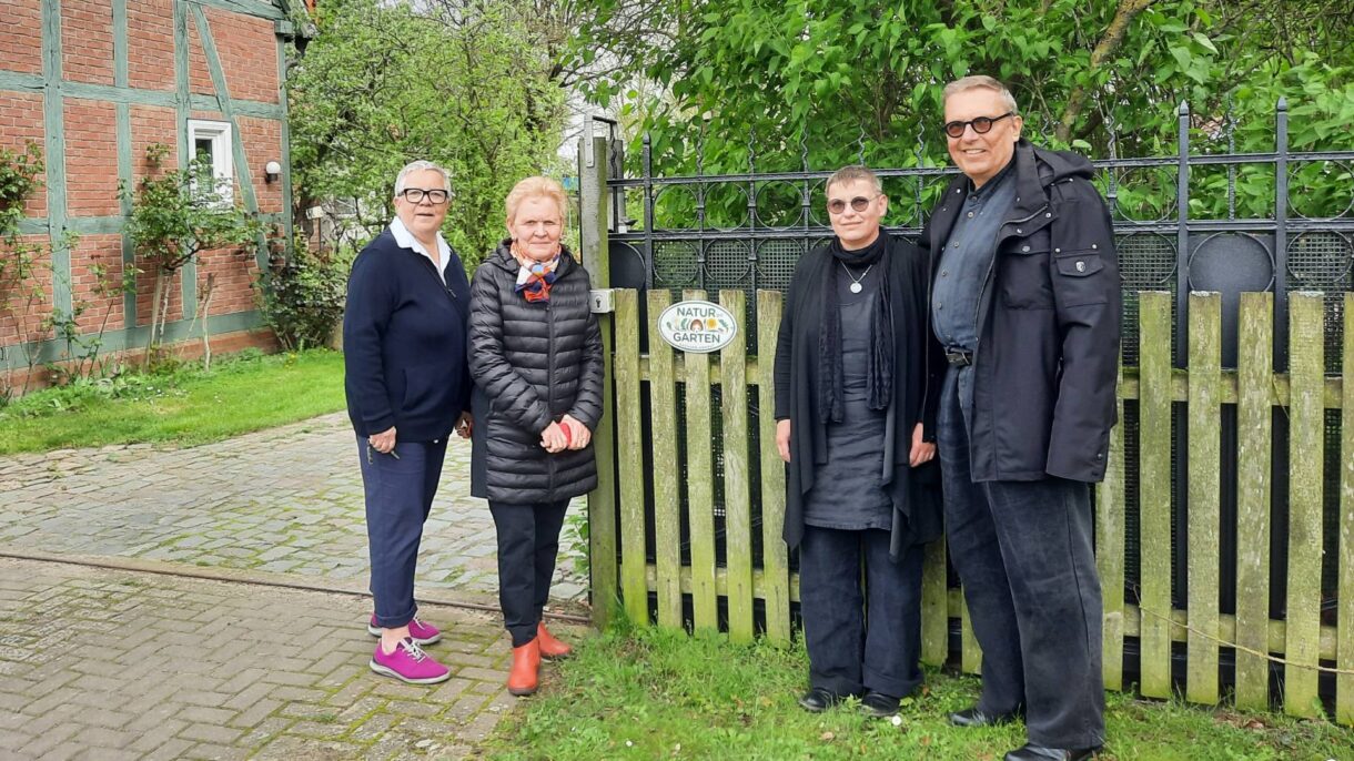 3 Frauen und ein Mann vor einem Zaun mit der Plakette von "Natur im Garten"